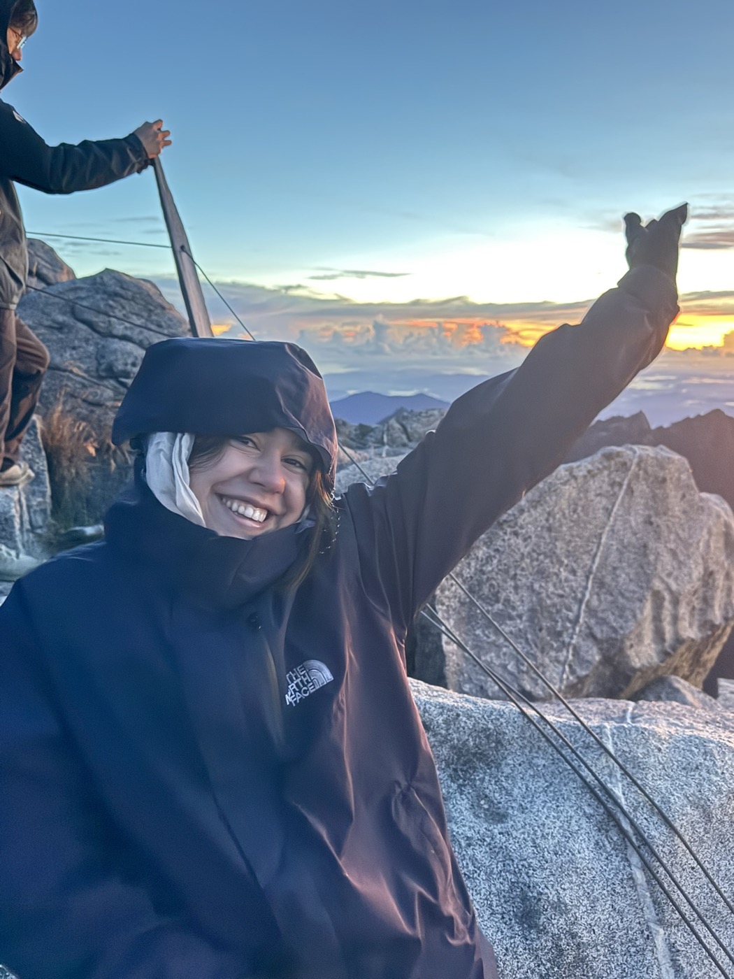 Alix smiling at sunrise on the summit of Mount Kinabalu, arm raised to the sky.